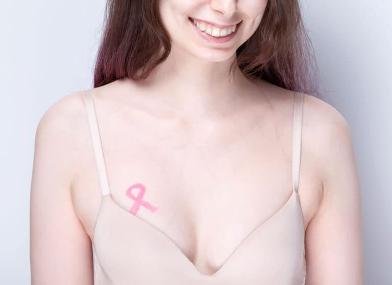 Brustkrebs Vorsorge_Frau mit pinker Schleife auf der Brust lächelnd